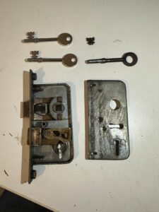 Mortice lock from a 40 year old aluminium balcony door opened up on the bench, shown with the snapped original ring key and two new keys cut to it